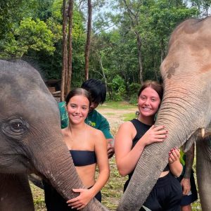 Thailand group tour with two girls stood next to elephants